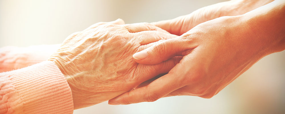 younger hands reaching out and holding hands of an older person